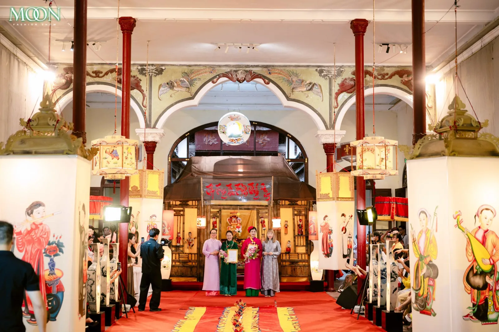 Models showcase traditional attire on a vibrant runway at the Moon Fashion Show 2025 inside a decorated hall.