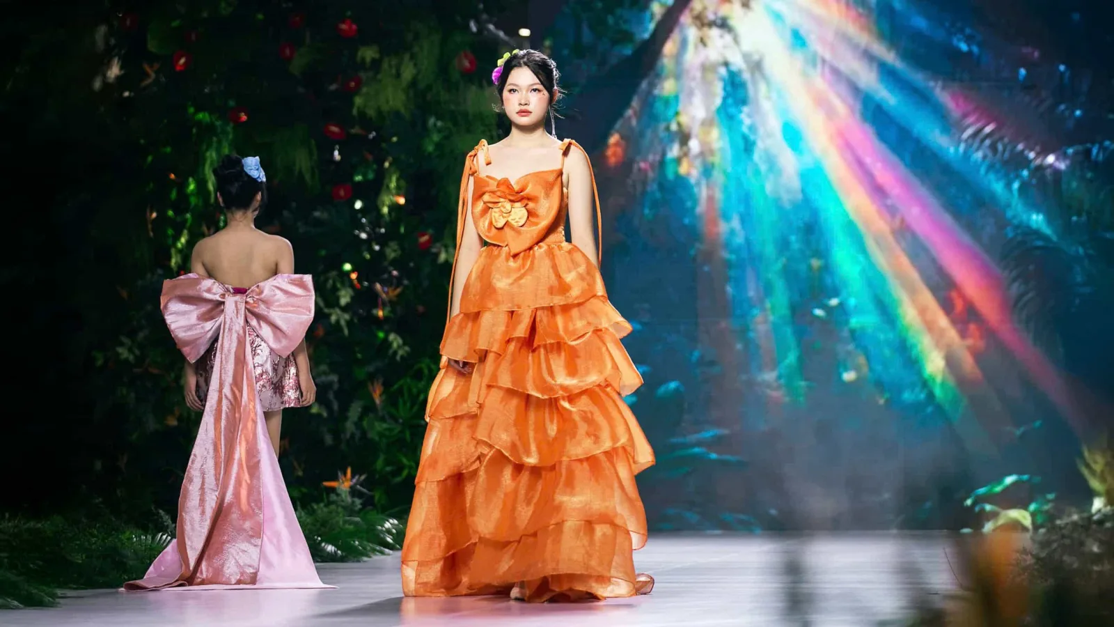 Models in vibrant gowns walk the runway under rainbow lights, showcasing the fashion designs of Vũ Phạm Giáng Vân.