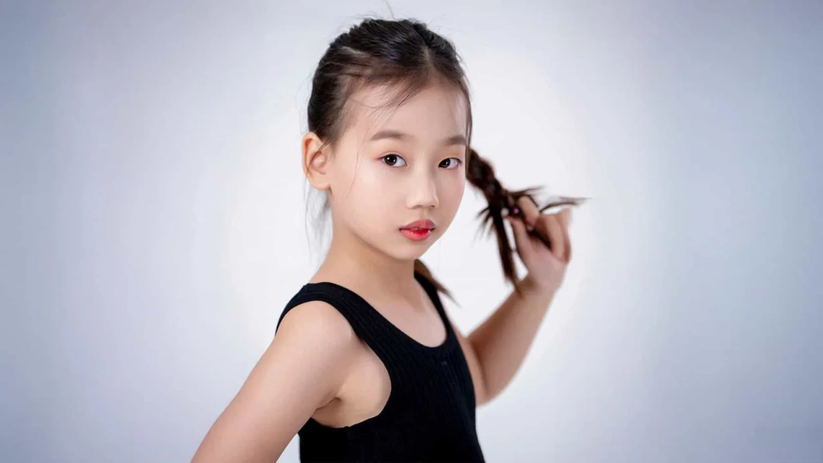 Đặng Huyền Anh posing confidently in a black sleeveless outfit, holding her braided hair against a light background.