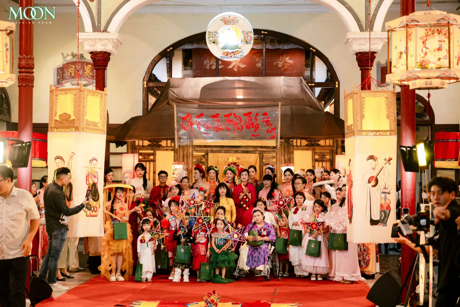 Group of models in traditional attire pose with lanterns and fans at the Moon Fashion Show 2025 cultural event.