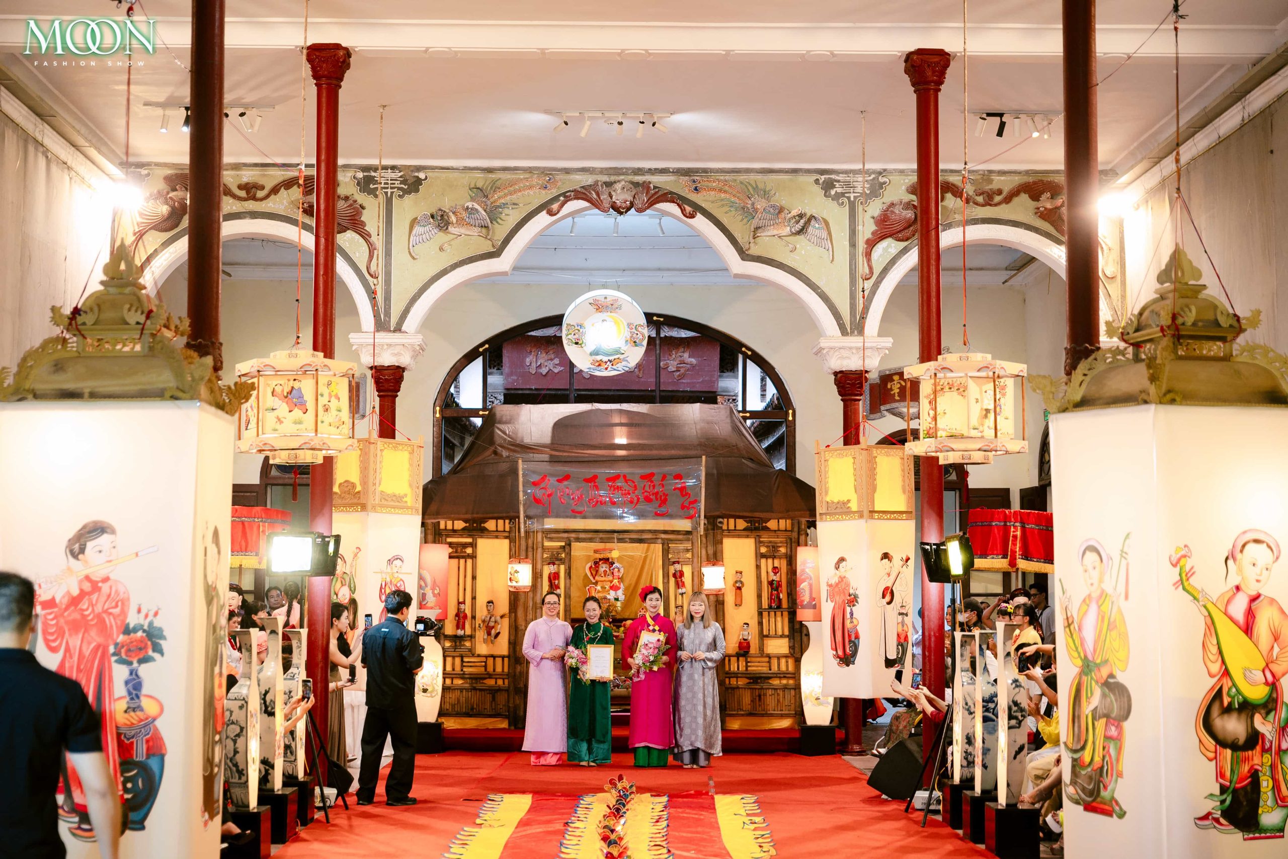 Models showcase traditional attire on a vibrant runway at the Moon Fashion Show 2025 inside a decorated hall.